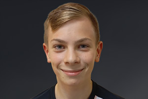 Junger Mann mit kurzen, blonden Haaren und einem freundlichen Lächeln vor einem dunklen Hintergrund.