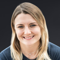 Porträt von Iris Schmiedbauer mit lächelndem Gesicht und blonden Haaren auf dunklem Hintergrund.